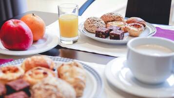Una mesa de desayuno con platos de pasteles, una manzana, una naranja y un vaso de zumo de naranja.