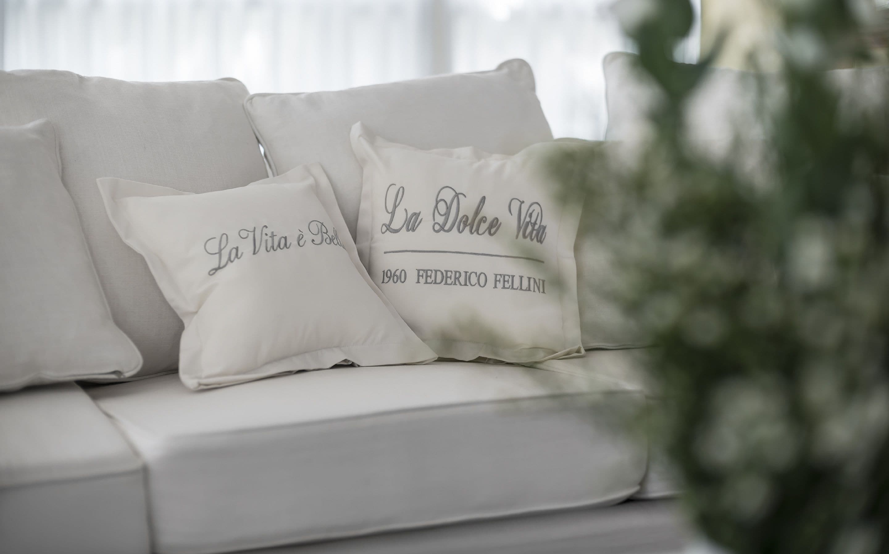 A white sofa with two decorative pillows, one with text and the other with a name and date.