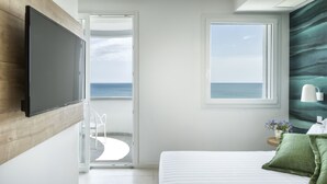 A bedroom with a bed, a TV mounted on the wall, a window with a view of the sea, and a balcony with a chair. - Hotel Meeting (Riccione)