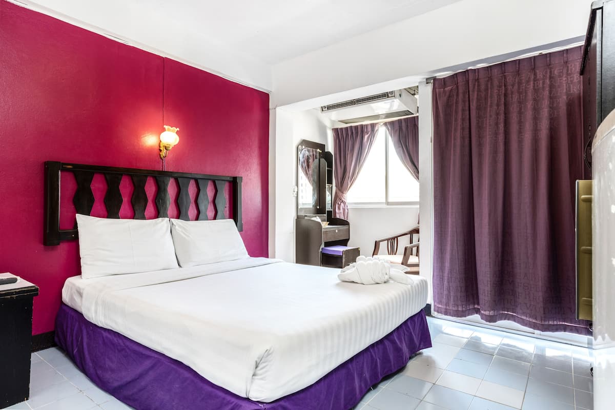 A hotel room with a bed, a nightstand, a desk, and a window with purple curtains.