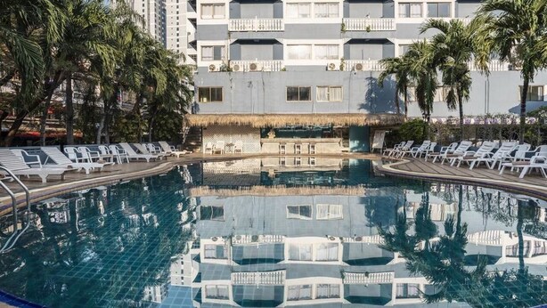 A swimming pool with lounge chairs, palm trees, and a building with balconies in the background. - Sawasdee Pattaya (Pattaya)