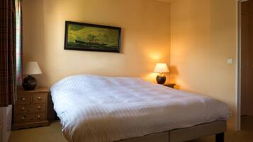 A bedroom with a large bed, two bedside tables, a lamp, a painting on the wall, and a door.