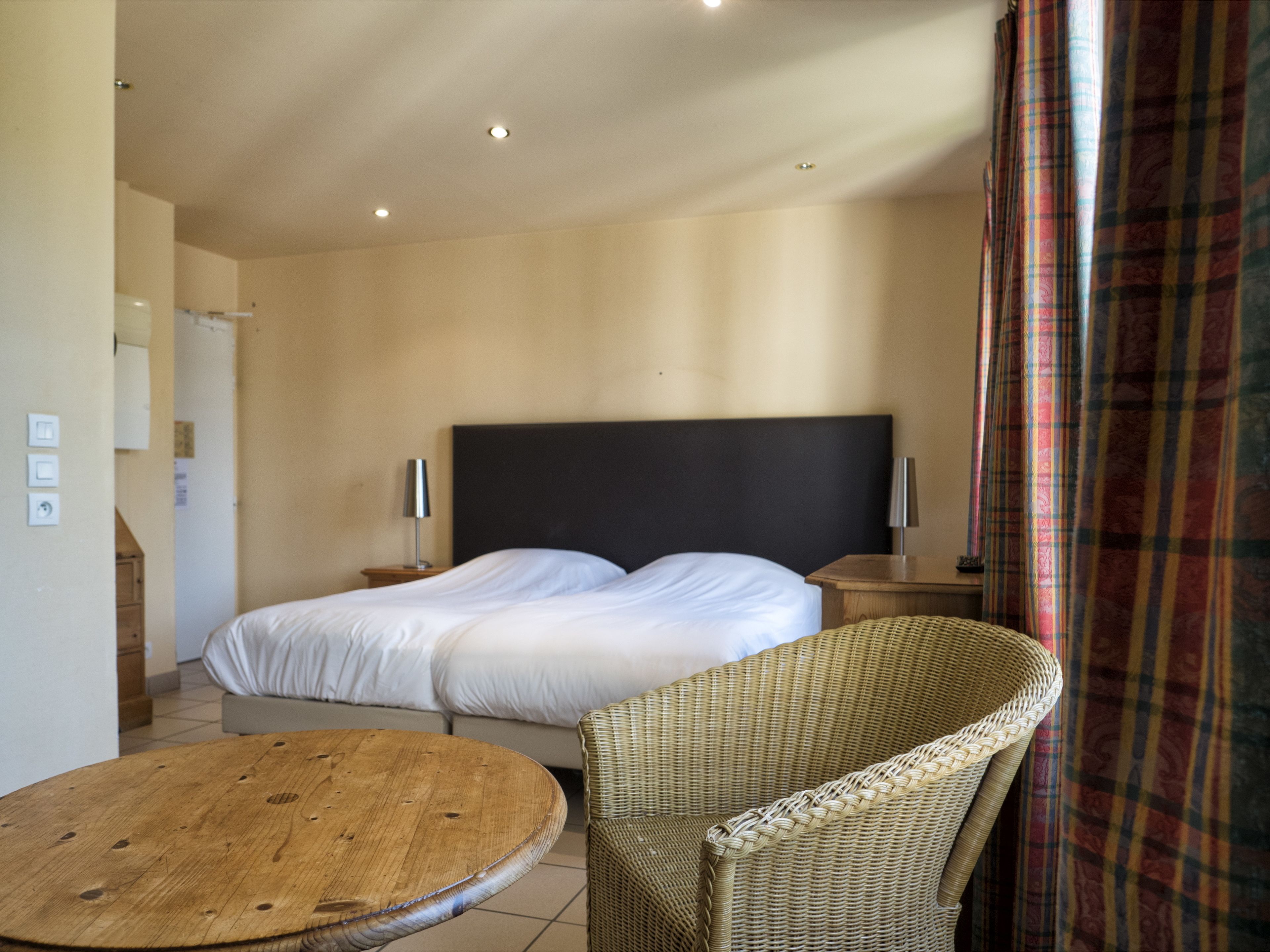 Una habitación de hotel con una cama grande, dos lámparas de noche, una silla de mimbre y una mesa de madera.
