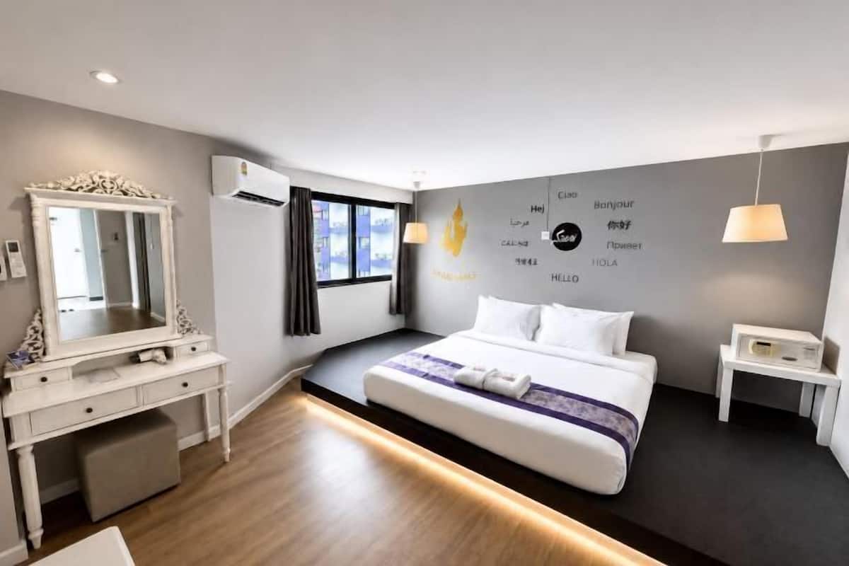 Habitación de hotel moderna con una cama grande, un tocador con espejo, un escritorio y un aire acondicionado de pared.