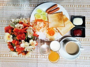 A breakfast plate with toast, hot dogs, and vegetables, a cup of coffee, and a floral arrangement.