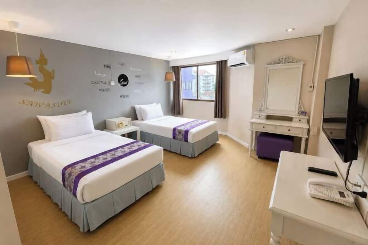 Quarto de hotel com duas camas, uma escrivaninha com computador, televisão e janela com vista para edifícios.