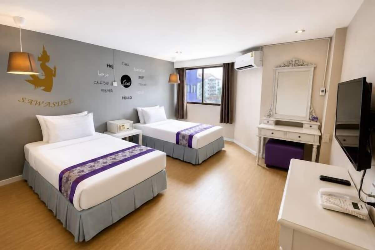 Habitación de hotel con dos camas, un escritorio, televisor, espejo y ventana con cortinas.