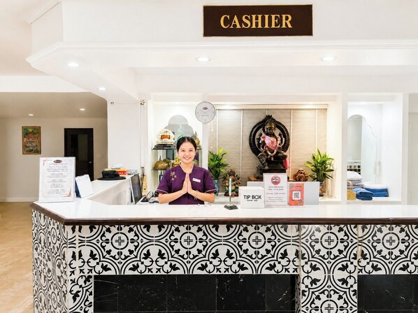 Un comptoir d’accueil avec une pancarte indiquant « CAISSE », une autre pancarte indiquant « POUR-BOIRE » et une statue en arrière-plan.