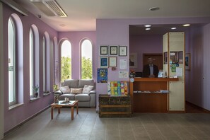 A reception area with a wooden desk, a sofa, and a large window with arched tops. - Hotel Manora (Mali Losinj)