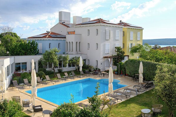 A hotel with a swimming pool, lounge chairs, and umbrellas. - Hotel Manora (Mali Losinj)