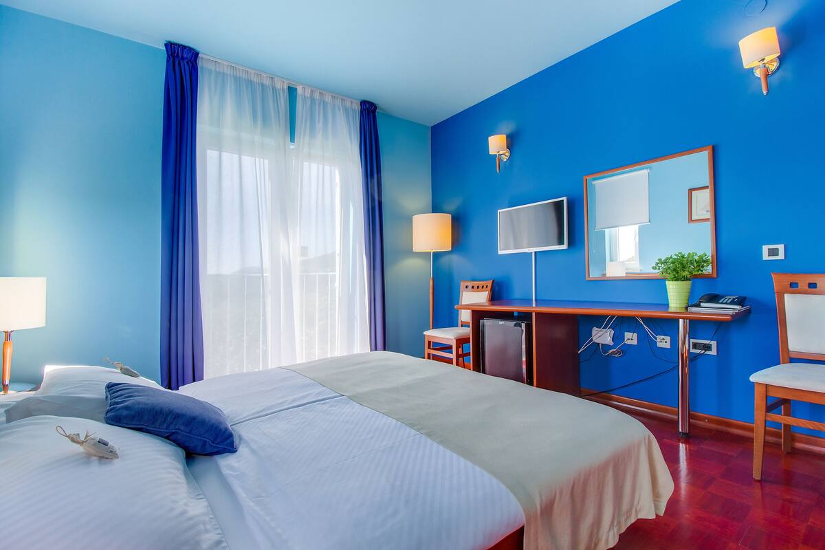 A hotel room with a large bed, a desk with a computer, a chair, a TV, and a mirror.