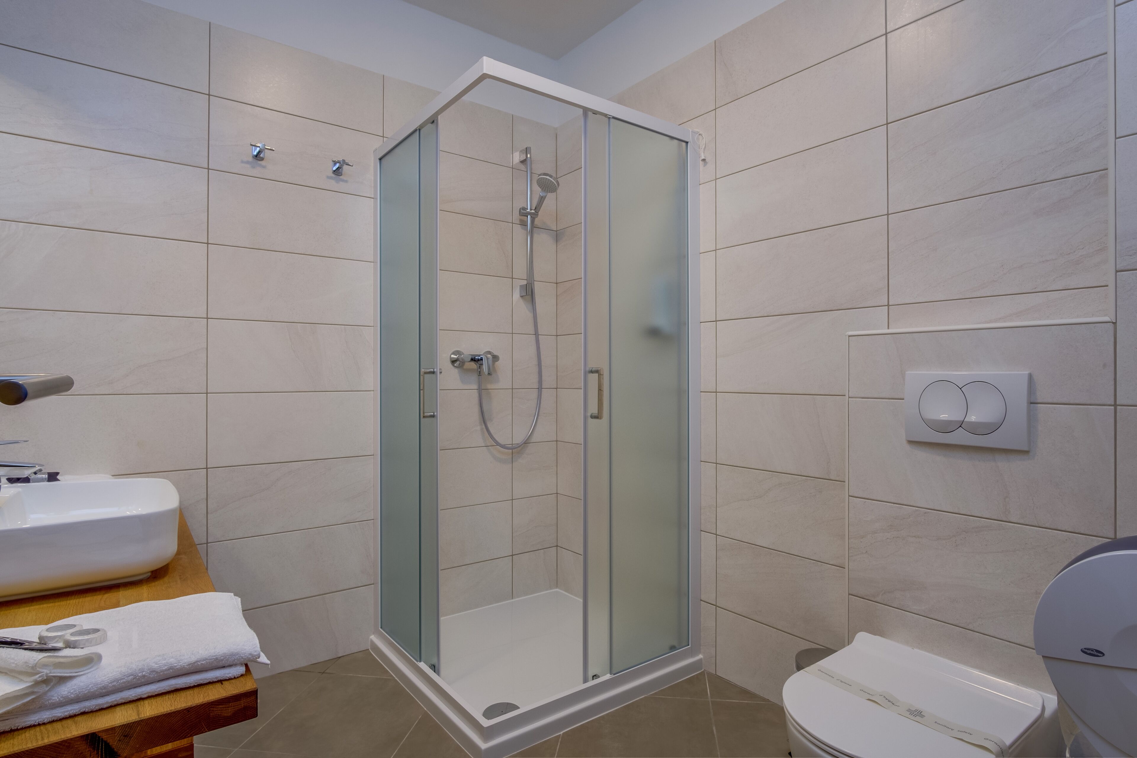 Een moderne badkamer met een douche met glazen wand, een witte wastafel en een toilet.