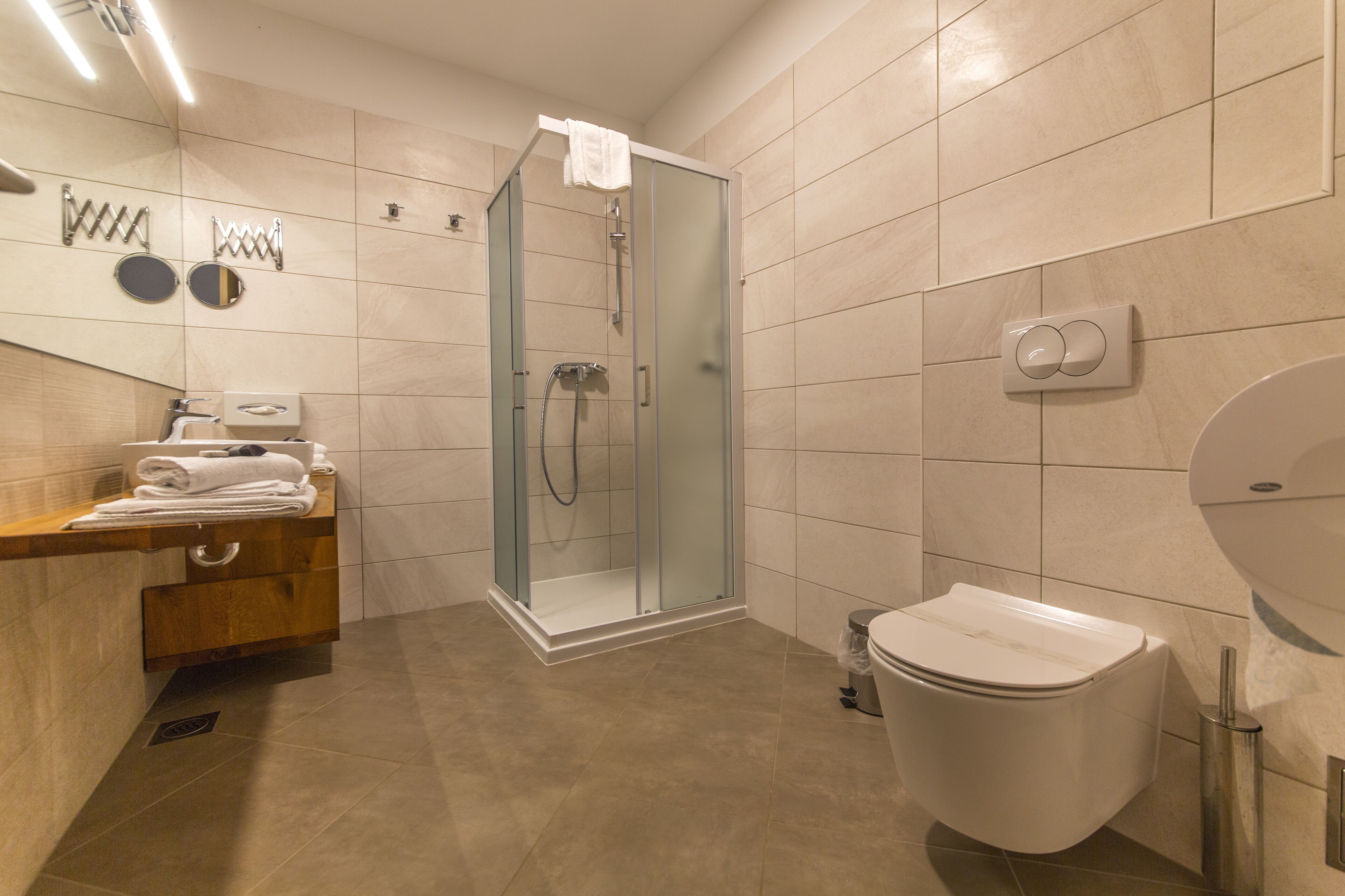Ein modernes Badezimmer mit einer einteiligen Duschkabine, Toilette und einem Waschbecken mit Holzablagefläche.