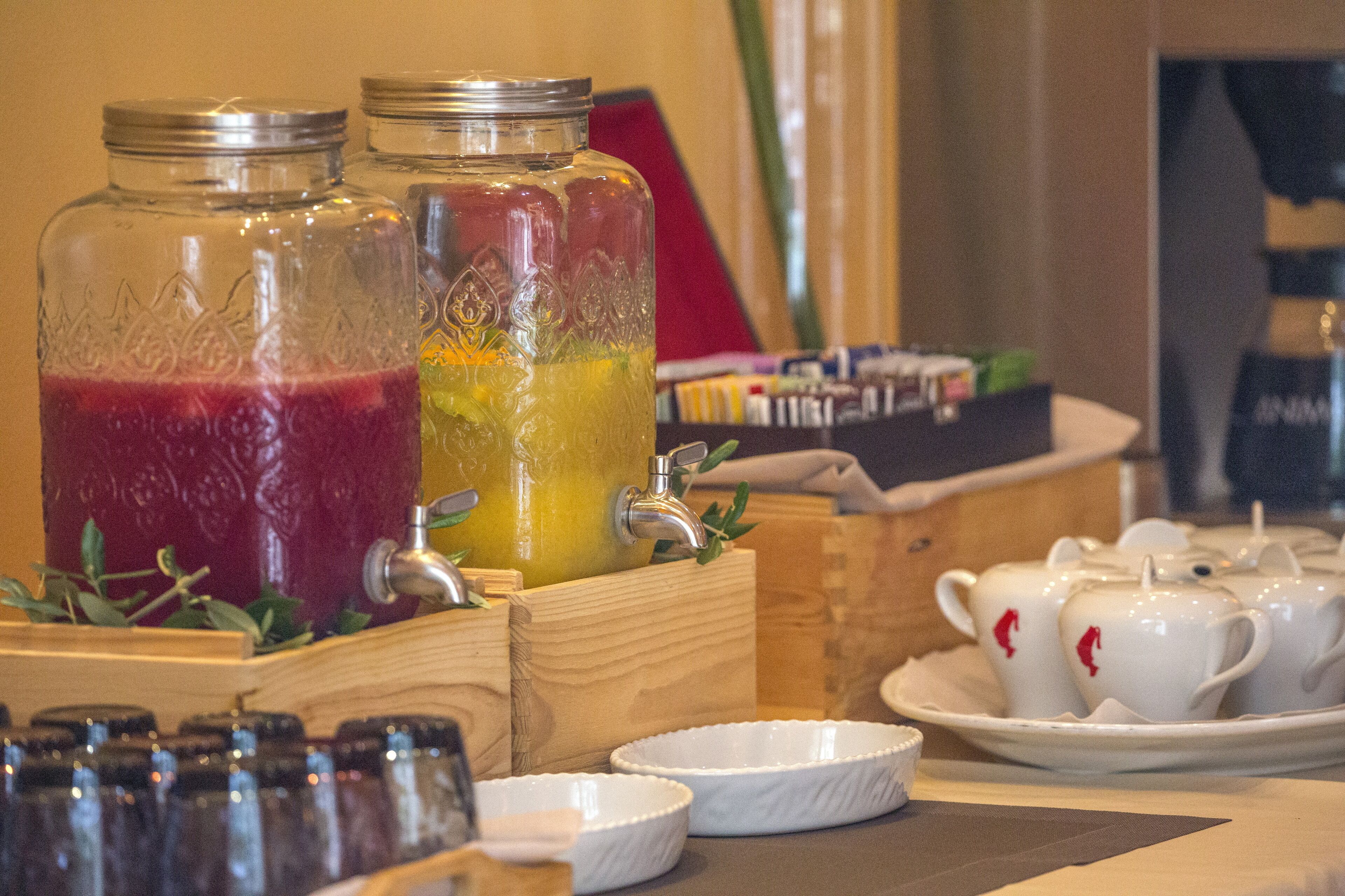 Un coin boissons comprenant deux grands bocaux en verre remplis de boissons, une boîte en bois contenant des tasses à thé et un plateau avec des théières.