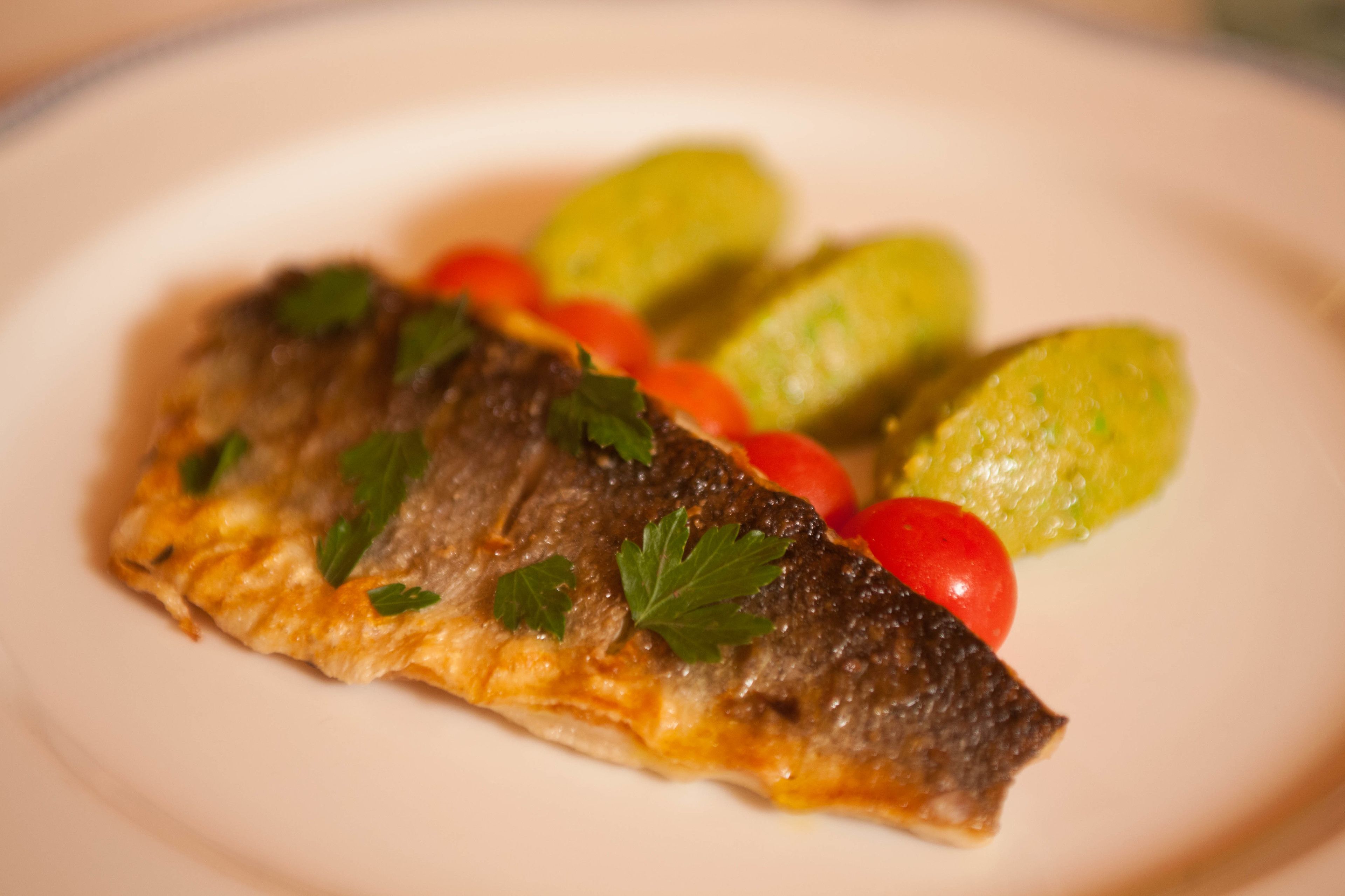 A plate with a fish fillet, cherry tomatoes, and pickles.