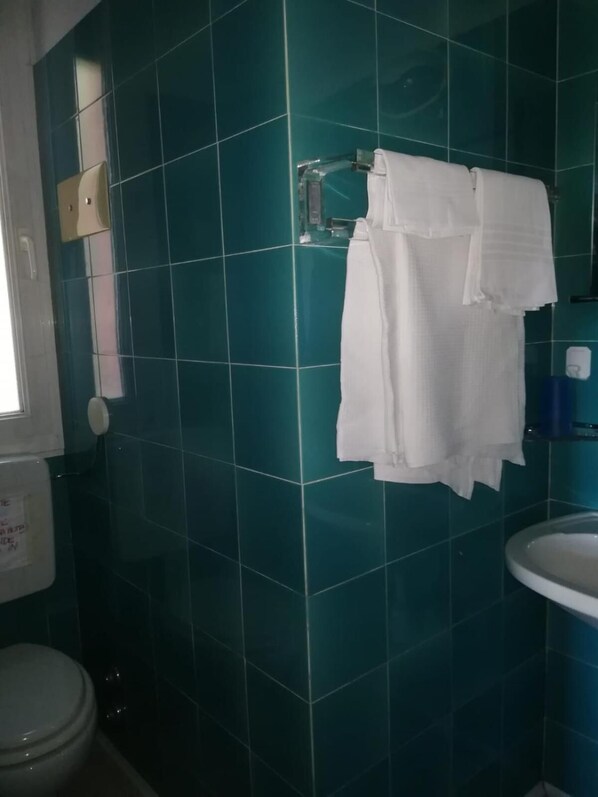 Un baño con azulejos color turquesa, un lavamanos blanco y un inodoro.