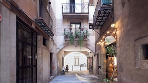 Una calle estrecha con un edificio a la izquierda, un balcón con plantas y una tienda a la derecha.