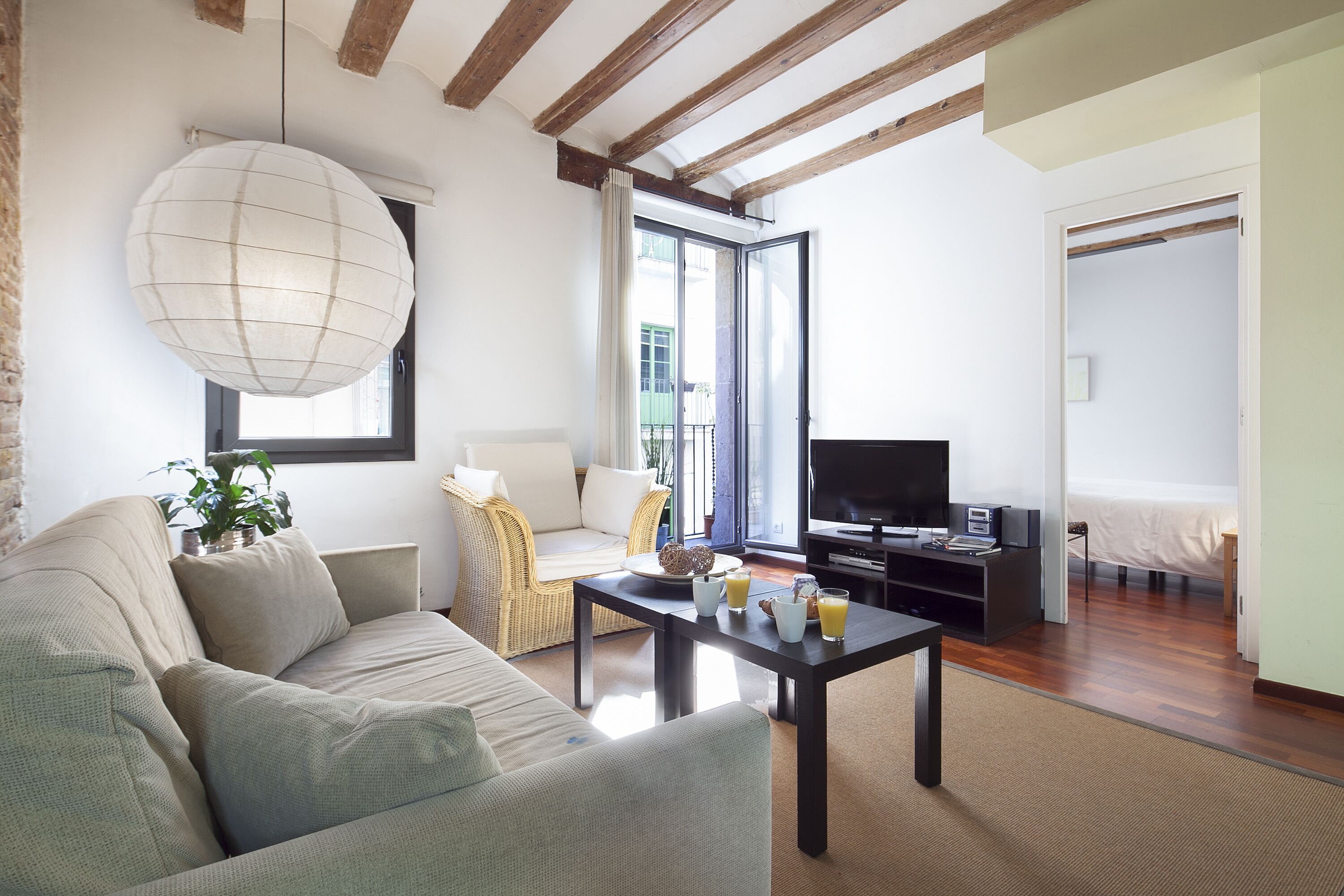 Un salon moderne avec un canapé, une table basse et un téléviseur. Il y a un balcon avec vue sur l’extérieur.