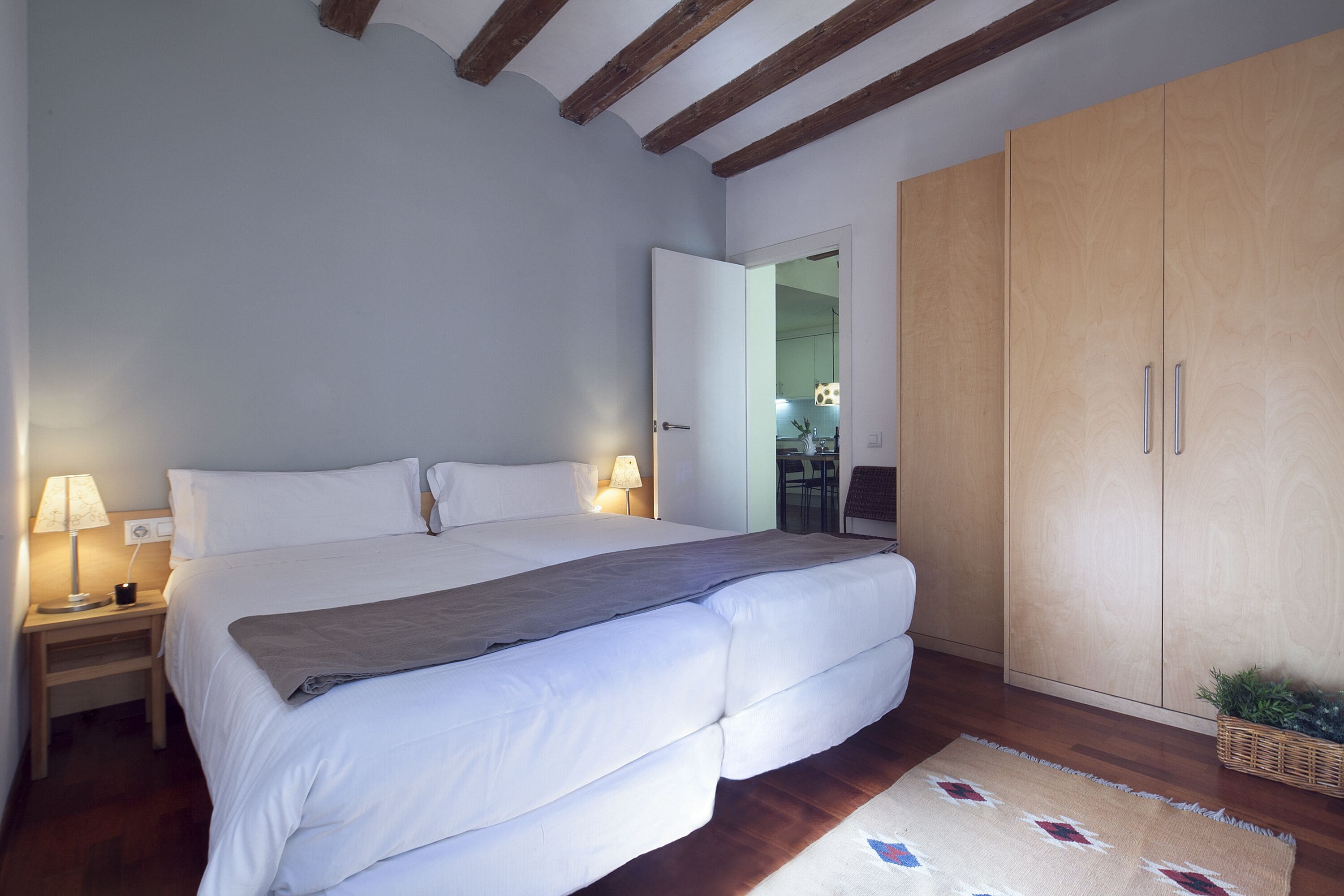 A bedroom with a large bed, wooden wardrobe, and a nightstand with a lamp.