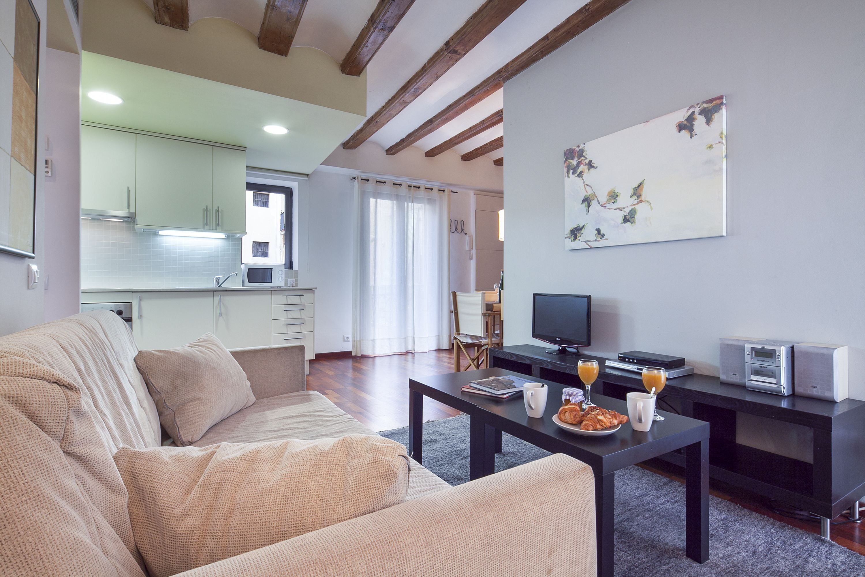 A modern living room with a sofa, a coffee table with breakfast items, a TV, and a kitchen in the background.