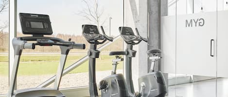 A gym with treadmills and elliptical machines, large windows, and a view of a grassy field.