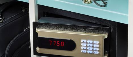 Un mini bar con cerradura digital y teclado, una maleta negra y un estante color turquesa con libros y una cámara.