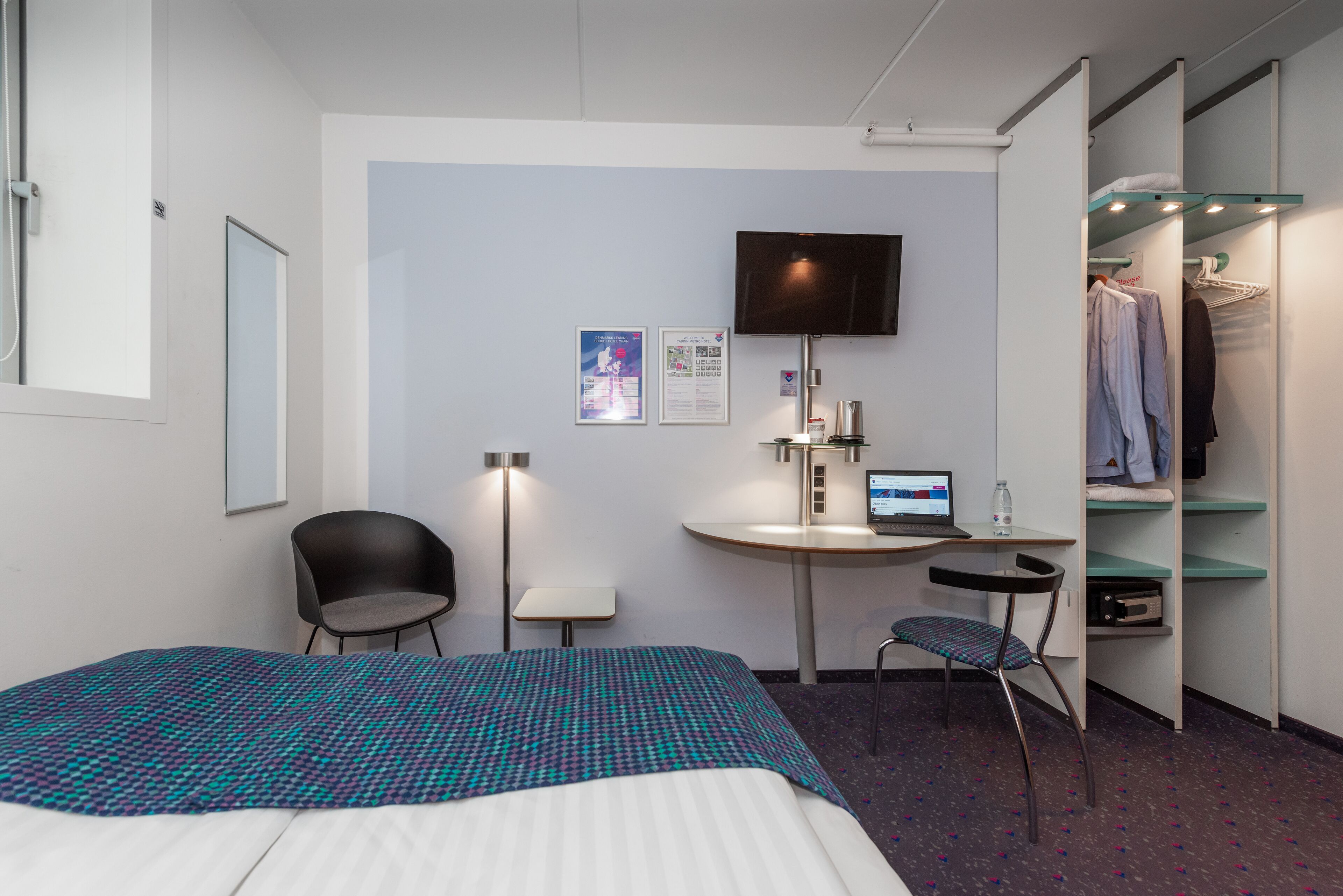 Een hotelkamer met een bed, een bureau met een computer, een stoel, een televisie en een kledingkast.