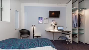 Et hotelværelse med en seng, et skrivebord med computer, en stol, et fjernsyn og et klædeskab.
