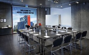 A conference room with a large screen displaying a welcome message, multiple tables with chairs, and a whiteboard. - CABINN Metro Hotel (Copenhagen)