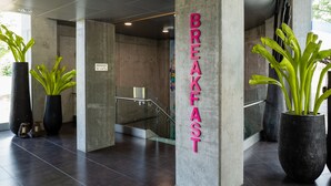 Interior de un edificio moderno con un cartel que dice 'BREAKFAST' y plantas en macetas.