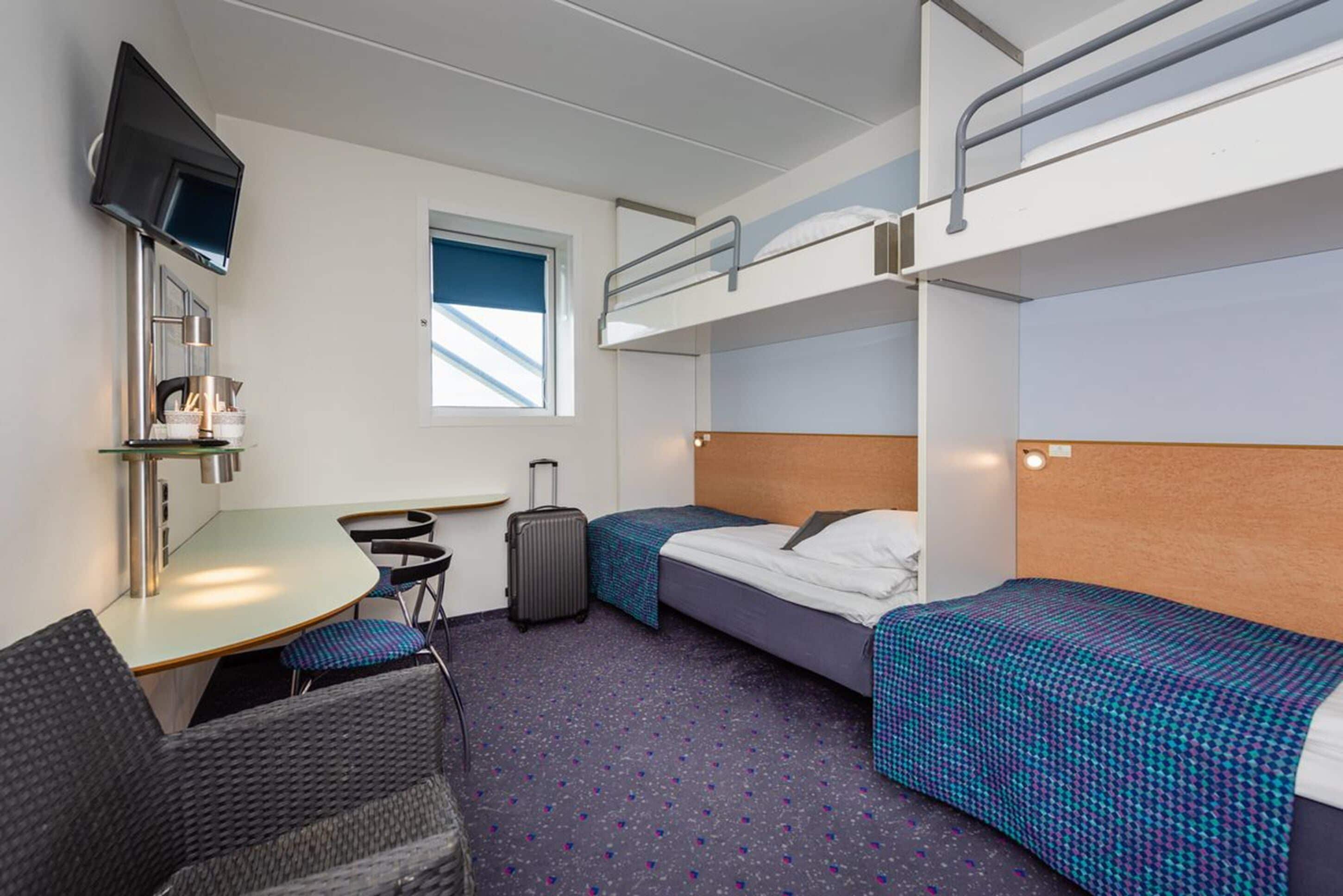 Een hotelkamer met stapelbedden, een bureau met stoel, een kleine tafel, een televisie en een raam met uitzicht.