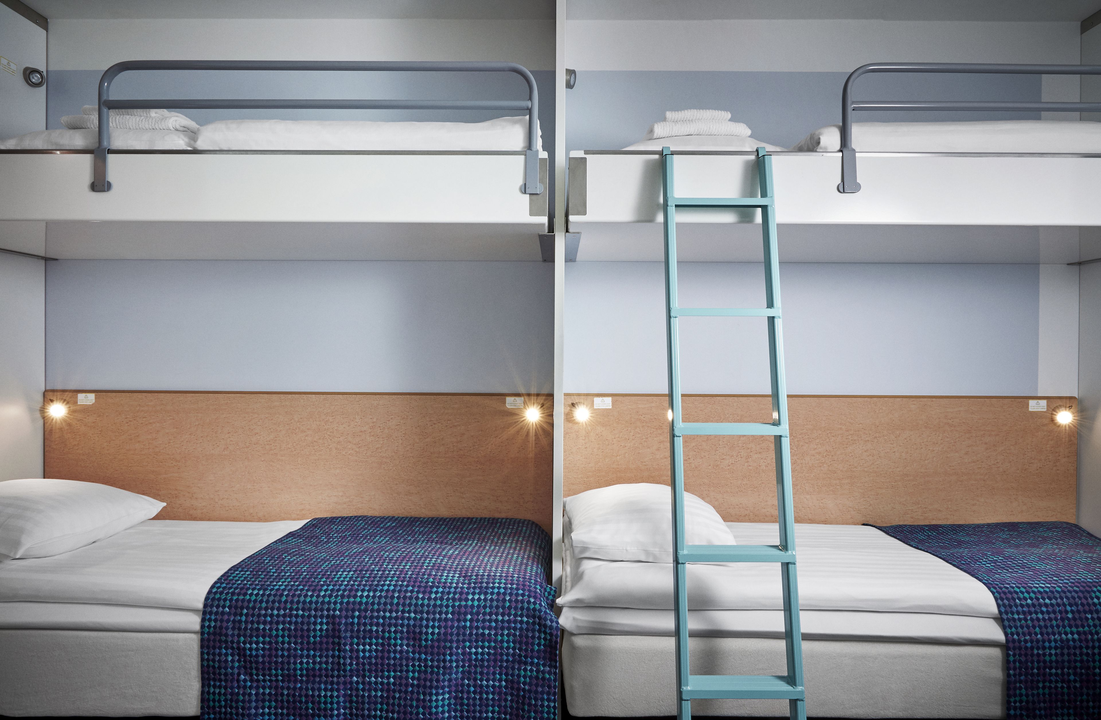 A hotel room with two beds, a wooden headboard, and a ladder between them.
