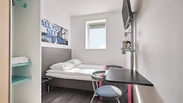 Una habitación pequeña con cama, escritorio, silla, televisor y ventana.