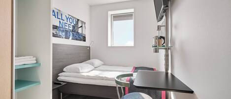 A compact room with a bed, a desk, a chair, a TV, and a window.