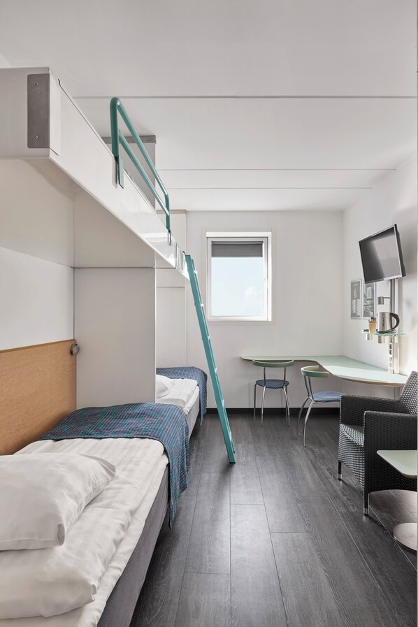 Habitación de hotel pequeña con una cama individual superior e inferior, un escritorio con silla, televisión y ventana.