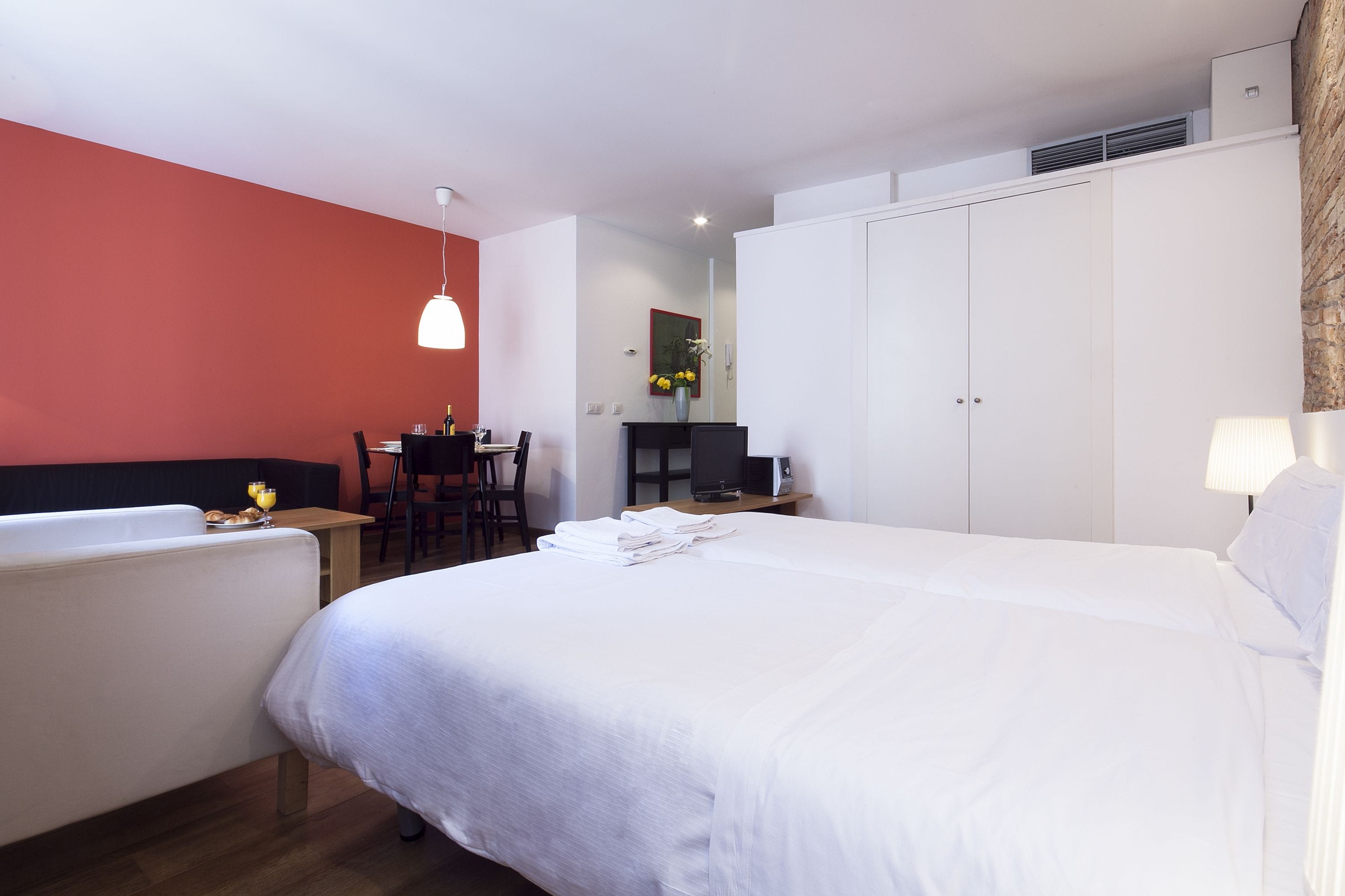 A hotel room with a bed, a desk, a chair, a lamp, and a wardrobe.