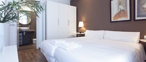 Ein Hotelzimmer mit einem großen Bett, einem weißen Wandschrank, einem Badezimmer mit Waschbecken und Spiegel sowie zwei gerahmten Kunstwerken an der Wand.