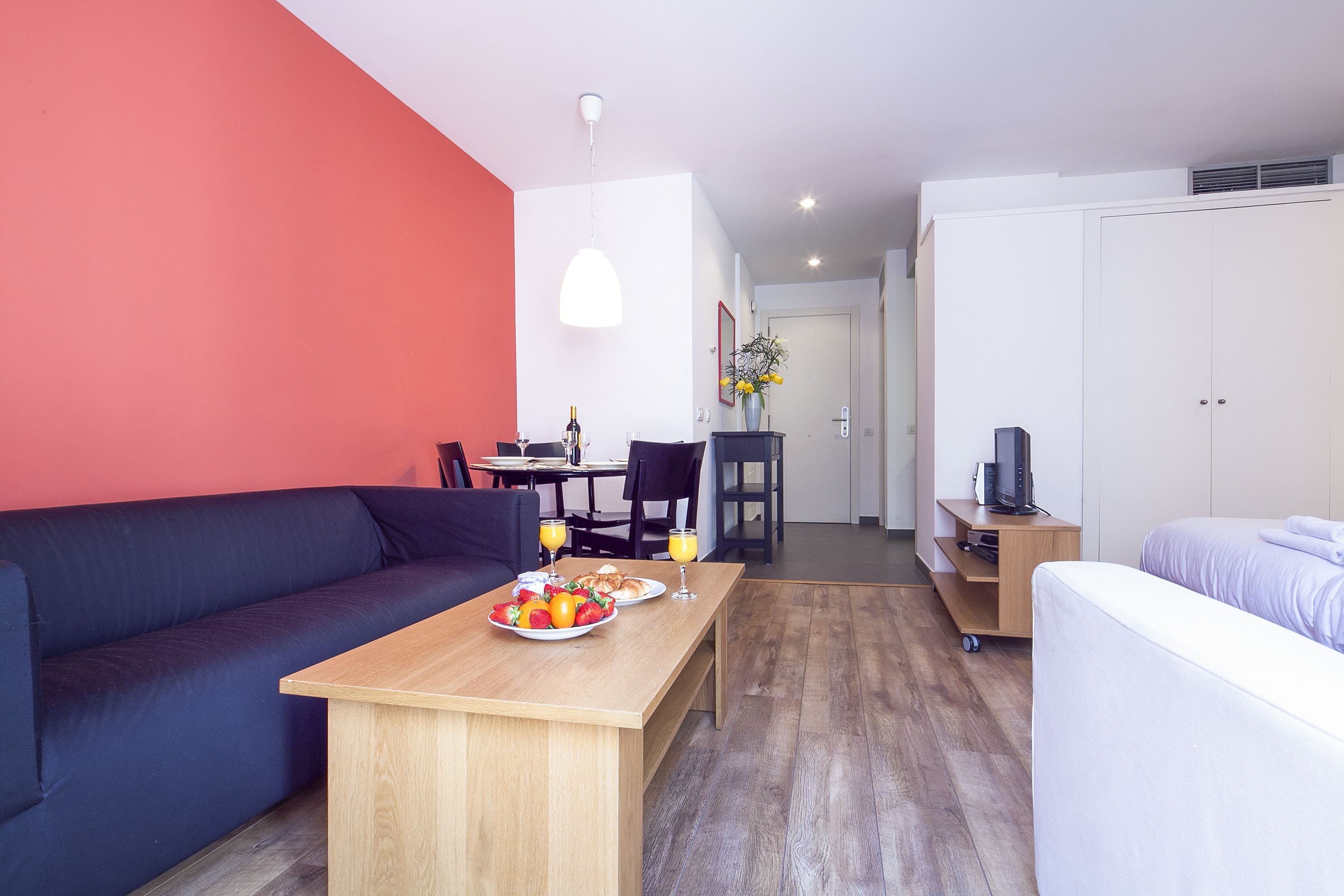 A modern living room with a sofa, a wooden table with breakfast, a TV, and a wardrobe.