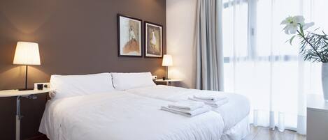 A hotel room with a large bed, two bedside lamps, a small table, and a window with curtains.