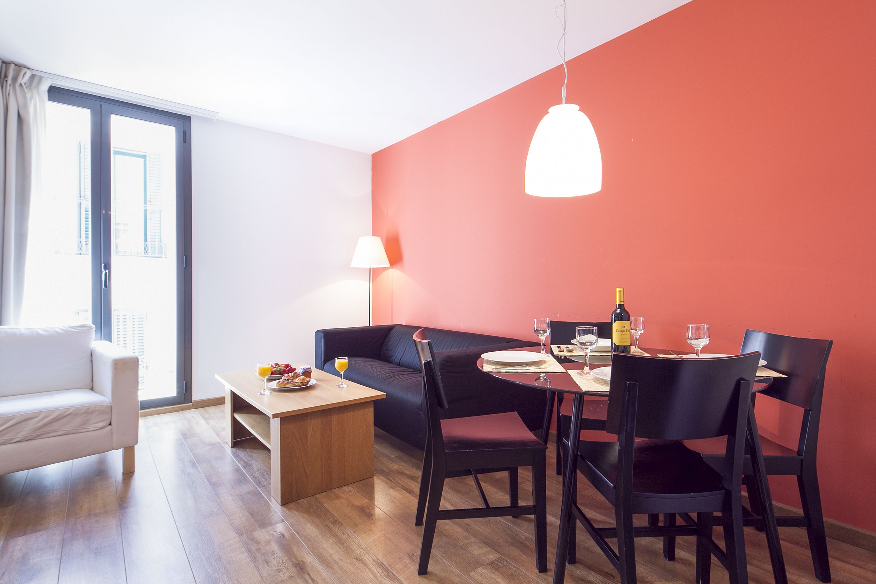 Una sala de estar moderna con comedor, que incluye un sofá, una mesa de comedor con sillas, una lámpara y una botella de vino.