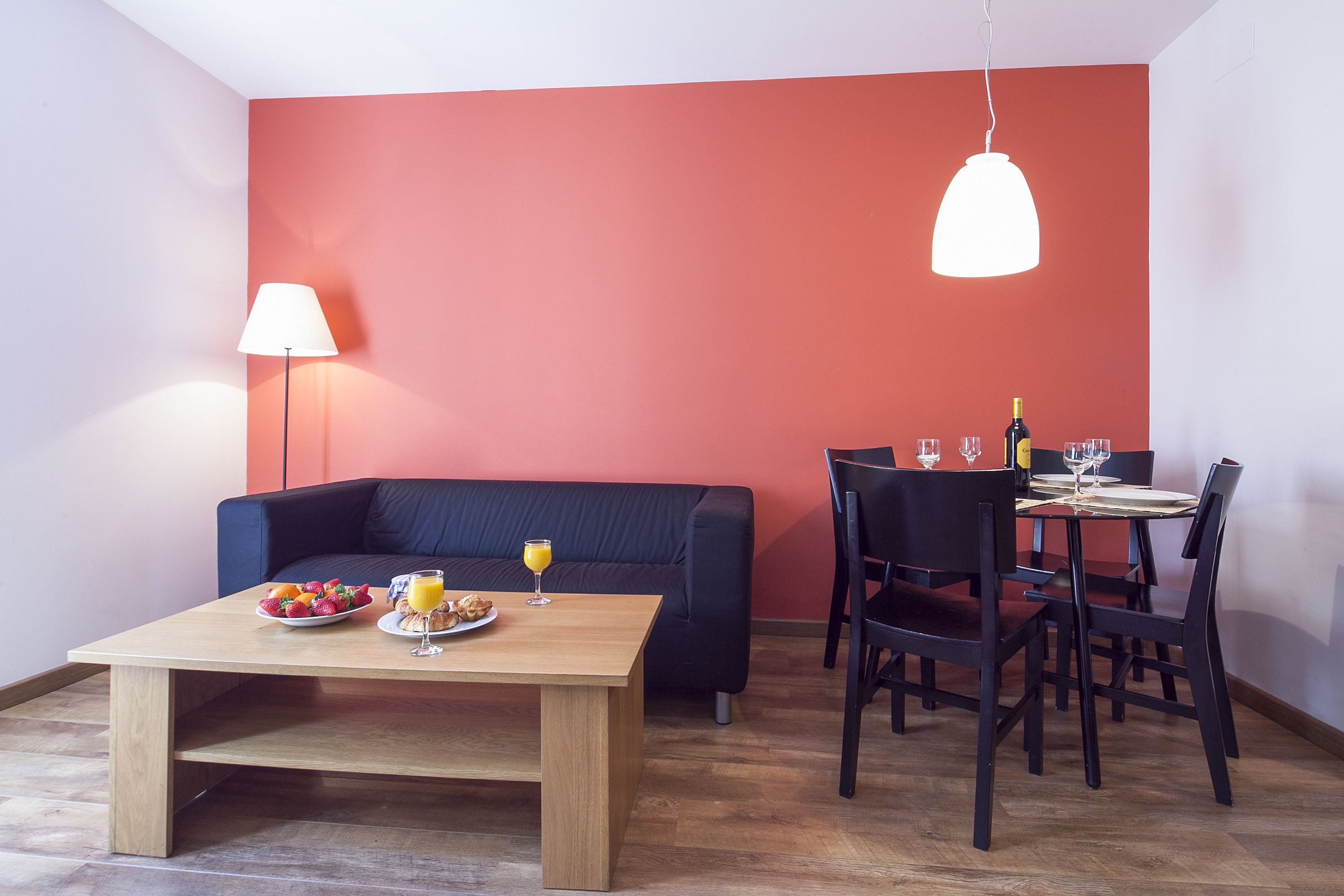 Un salon moderne avec un canapé, une table à manger et des chaises. On peut voir une lampe, une bouteille et un verre de jus d’orange sur la table.