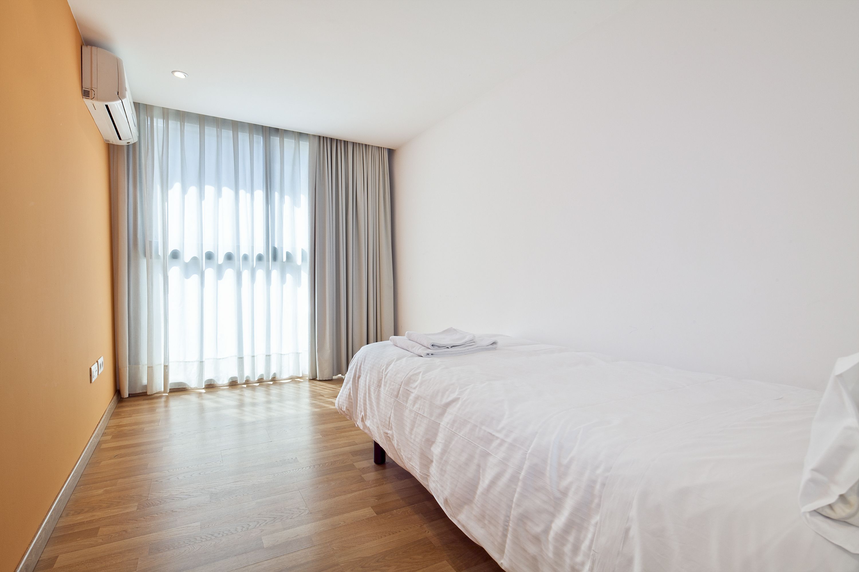 A hotel room with a large bed, a window with curtains, and an air conditioning unit on the wall.