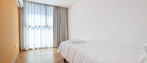 A hotel room with a large bed, a window with curtains, and an air conditioning unit on the wall.
