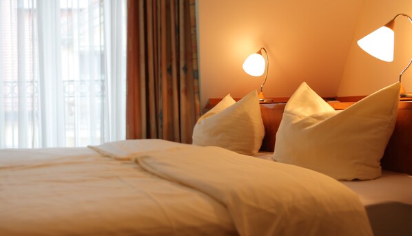 A hotel room with a neatly made bed, two bedside lamps, and a view of the outdoors through large windows. - Hotel Am Klostergarten (Freising)