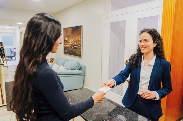 Een hotel receptie met een receptiebalie, een lichtblauwe bank en een ingelijste foto aan de muur.