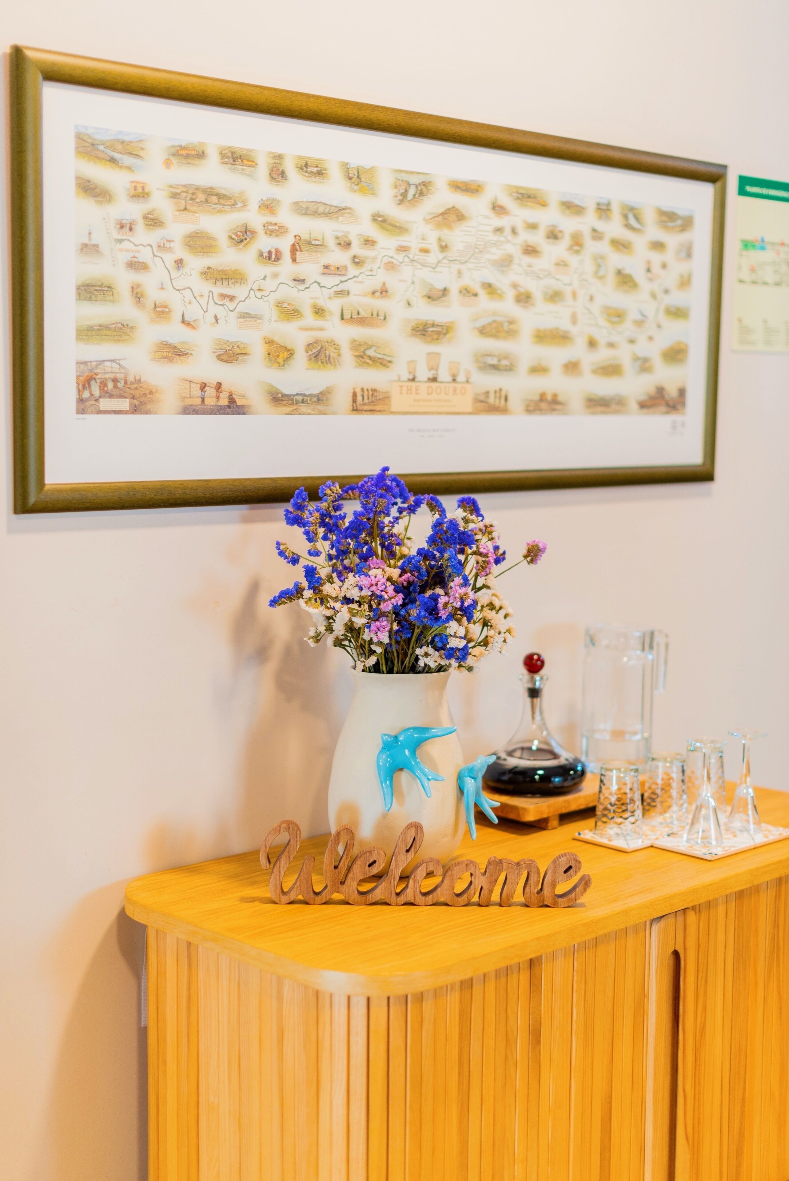 A reception desk with a framed map, a vase of flowers, a bottle, and a 'Welcome' sign.
