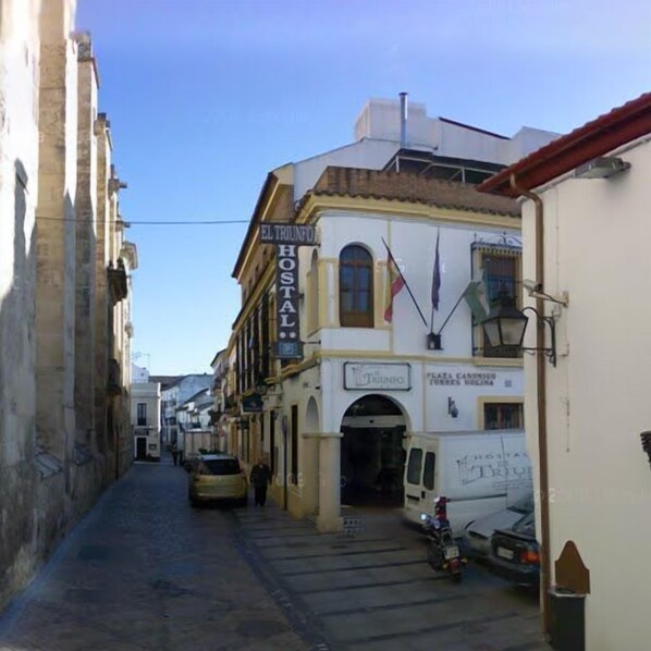 A narrow street with a building labeled "EL TRUNFO HOSTAL" and a sign for "PLATA CANONICA TORRES VOLONTA". - El Triunfo (Córdoba)