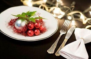A plate with a decorative arrangement of red berries and a green leaf, accompanied by a folded white napkin and silverware on a dark surface. - El Triunfo (Córdoba)