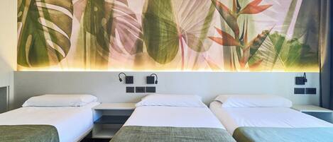 A hotel room with three beds, a large tropical leaf mural on the wall, and bedside lamps.