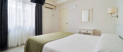 A hotel room with a bed, a TV, a ceiling fan, a window with curtains, and a bedside table.